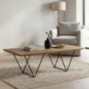 A modern light wood coffee table with geometric wireframe legs, set in a styled neutral living room corner.